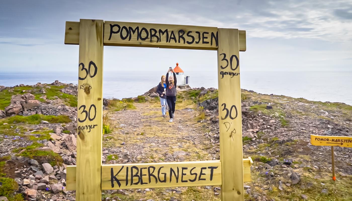 Ungdom tar bilder på toppen av Domen-fjellet. Vi ser dem gjennom en treramme som er laget for at folk skal ta bilder.